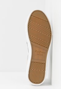 Bílá podrážka tenisky s texturovaným hnědým gumovým vzorem. Obsahuje vulkanizovaný design a značení na mezipodešvi.