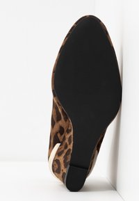 Chaussure à talon haut imprimé léopard avec une tige en suède, une semelle en caoutchouc noire, et un design à bout pointu. Remarquable par son motif texturé et le contraste des couleurs.