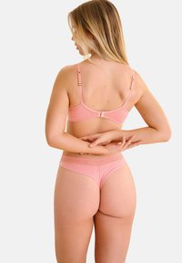 Ensemble de lingerie rose comprenant un soutien-gorge lisse avec des bretelles réglables et un string assorti avec des détails texturés au niveau de la taille.