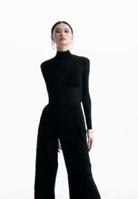 Svart tettsittende bodysuit med lange ermer og høy hals, kombinert med løse svarte bukser, som viser en strømlinjeformet silhuett og glatt tekstur.