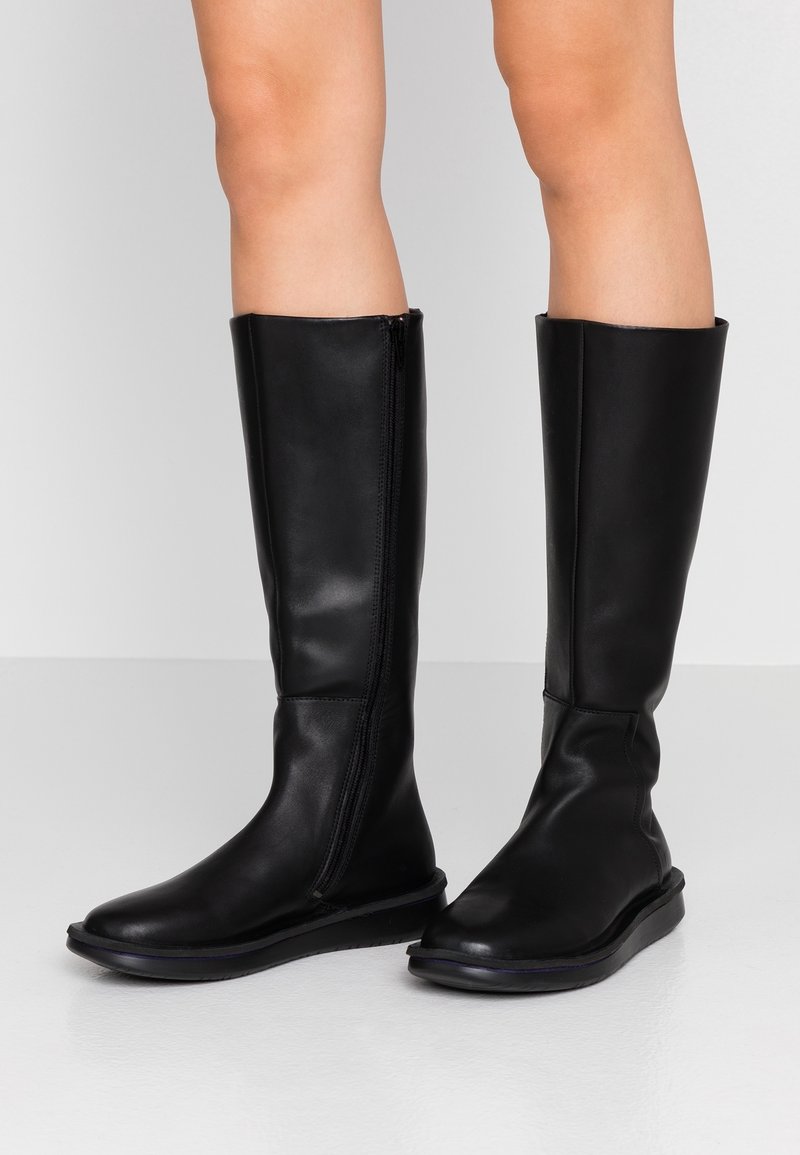 Stivali neri fino al ginocchio in pelle liscia. Presentano una zip laterale e una suola bassa e piatta. Design minimalista con una forma affusolata.