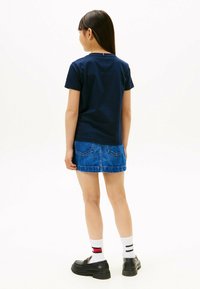 Marineblå bomulds T-shirt sammen med en blå denim miniskirt. Sorte loafers og stribede sokker er også påført. Synlige syninger og lommer.