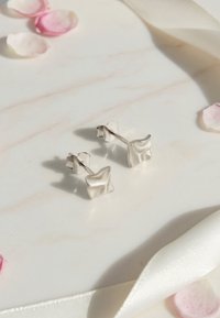 Silberne Steckerohrringe mit einem strukturierten, wellenförmigen Design, polierter Oberfläche und Steckverschluss, auf einer Marmoroberfläche platziert.