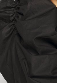 Indumento nero realizzato in morbido tessuto testurizzato, con dettagli arricciati e design fluido e drappeggiato. Nessun hardware o motivo visibile.
