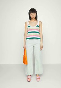 Top de malha com riscas verdes, rosas e brancas, combinado com jeans de perna larga de cor clara, bolsa laranja e sapatos de plataforma florais.