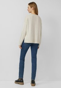 Hellbeiger Strickpullover mit lockerem Schnitt, gerippten Bündchen und Saum, kombiniert mit dunkelblauen, eng anliegenden Jeans und schwarzen Stiefeletten mit einer klobigen Sohle.