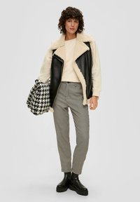 Zwarte en crèmekleurige shearling-voeringen gilet, crèmekleurige sweatshirt, houndstooth-gepatrooneerde broek en zwarte platform enkellaarsjes. Houdt een houndstooth tas vast.