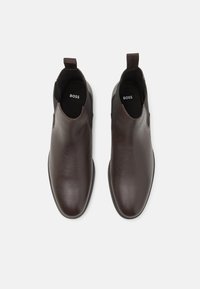 Bottines en cuir marron avec des panneaux élastiques sur les côtés, forme à bout d'amande et texture lisse. Présente le logo "BOSS" sur la semelle intérieure.