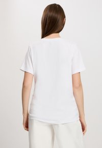 Biała koszulka z krótkim rękawem o luźnym kroju. Miękki materiał bawełniany z okrągłym dekoltem i gładką teksturą. Czysty, minimalistyczny design.