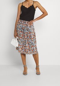 Svart cami med spetskant i kombination med en blommig, plisserad midikjol i blått, orange och vitt. Vit handväska och ljusblå klackar.