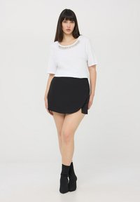 Biała bluzka z krótkim rękawem i wykończeniem z koralików, zestawiona z czarną spódnicą kopertową. Czarne botki dopełniają stylizację. Gładki materiał i nowoczesny design.