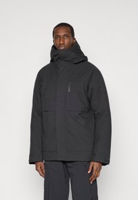 Czarna ocieplana kurtka z wysokim kołnierzem i regulowanym kapturem. Posiada duże kieszenie z przodu oraz teksturowany materiał.