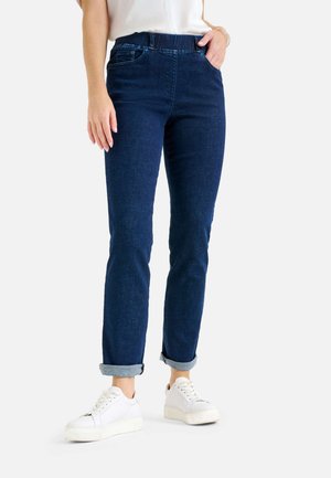 Jeans in denim blu scuro con gamba affusolata, risvoltati alle caviglie. Presentano tasche frontali e una vita comoda. Abbinati a sneakers bianche.