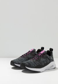 Baskets de sport noires et grises avec un dessus texturé, des lacets roses contrastants et une semelle blanche dotée d'un amorti à air.