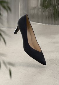 Black suede high-heeled shoe with a pointed toe and a sleek silver-accented heel. Smooth interior lining, minimalistic design.