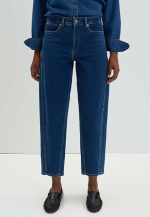 Blauwe denim jeans met een hoge taille, recht gesneden, en contraststiksel. Voorzien van zijzakken en ruwe zomen, gecombineerd met zwarte instappers.