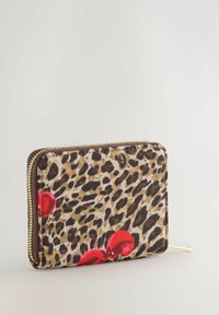 Portefeuille zippé avec imprimé léopard et accents de cerise rouges sur fond beige, présenté debout sur une surface claire.