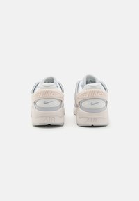 Nike Air-sneakers i ljusgrått och blekrosa, med en texturerad bakdel, vadderad krage och framträdande logotyp på hälen och remmen.