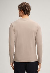 Beige Langarm-T-Shirt aus weichem Material, mit rundem Ausschnitt und einem dezenten eingravierten Logo auf der Rückseite. Glatte Textur, figurbetonte Passform.