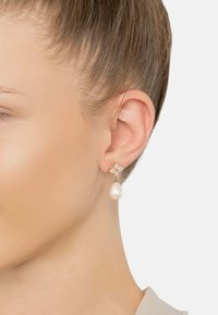 Gold-tone earrings feature a floral design with sparkling stones and a single teardrop pearl. The overall shape is elegant and refined.