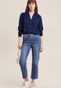 Marineblauwe blouse met lange mouwen, gecombineerd met lichtblauwe rechte jeans. Geaccentueerd met een zilveren handtas en witte sneakers.