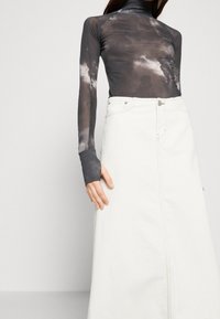 Musta ja harmaa sitruunapaita pitkällä hihalla, jossa on korkea kaulus, yhdistetty valkoiseen farkku-maxihameeseen, jossa on etusauma ja nappikiinnitys.