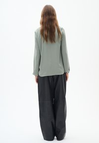 Blusa lunga a maniche corte verde chiaro con spalle a palloncino abbinata a pantaloni neri larghi. Tessuto morbido con una sottile trama e vestibilità rilassata.