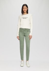 Bawełniana koszula z długim rękawem w kremowe i jasnoszare paski; zielone dopasowane dżinsy; białe sneakersy z teksturowaną podeszwą.