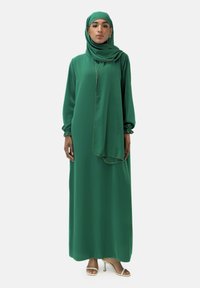 Grünes, langärmliges Kleid aus weichem Stoff, mit passendem Hijab, gerafften Bündchen und einem goldenen Akzent entlang des Schalrandes.