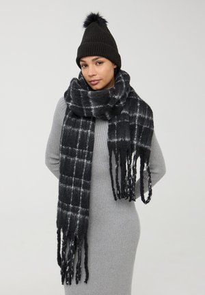 Berretto di maglia nera con pom pom e una sciarpa a quadri neri e grigi con bordi frangiati. La sciarpa ha un aspetto morbido e testurizzato.