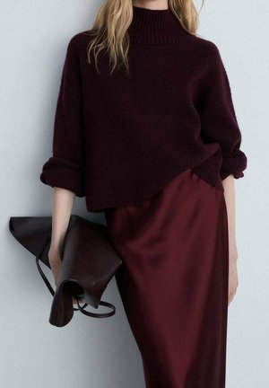 Oversized bordeaux trui met een hoge hals, gecombineerd met een bordeaux satijnen rok. Houdt een donkerbruine leren tas vast. Gladde textuur.