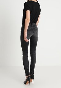 Jeans negros ajustados con una textura desgastada, de cintura alta y bolsillos traseros, combinados con tacones de aguja negros y una blusa negra de corte holgado.