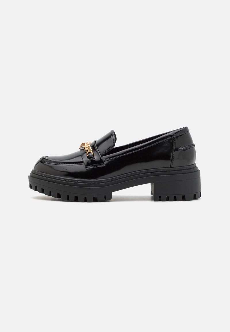Mocassin en cuir verni noir avec semelle à larges crampons et détail de chaîne dorée sur le dessus, présenté en profil latéral sur fond blanc.
