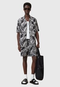 Camicia nera a maniche corte con motivo foglia bianca, pantaloni corto abbinati, canotta bianca, sandali neri e borsa a tracolla nera.