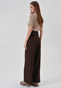 Beiges, geripptes Kurzarm-Top kombiniert mit braunen, weit geschnittenen Hosen mit hoher Taille und schmalem Gürtel-Detail. Braune Plateauschuhe runden das Outfit ab.