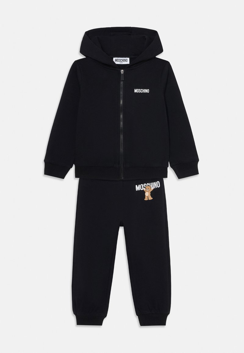 Melnais Moschino treniņtērps ar rāvējslēdzēju kapuci un elastīgu jostasvietu biksēm. Biksēm ir lāča grafika, bet uz kapuces ir logo teksts.