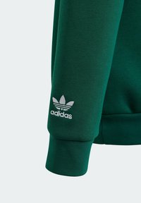 Grön sweatshirt med ribbad muddar, med en vit broderad Adidas-logga och det ikoniska tre-randsdesignen på ärmen.