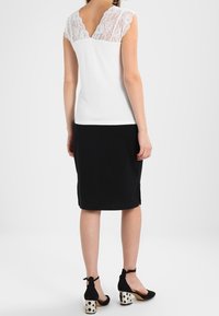 Vit topp med spetsdetaljer på axlarna, kombinerad med en svart pennkjol och svarta klackar med prickiga accenter.