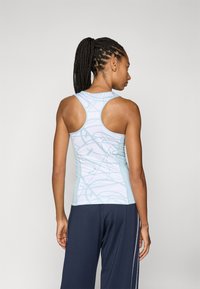 Top de treino azul claro com um padrão de linhas em espiral, apresentando um design de costas nadador e material suave e elástico. Combinado com calças escuras.