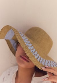 Cappello di paglia a tesa larga con fascia intrecciata blu e beige, che mostra un motivo texture e un colore marrone chiaro naturale.