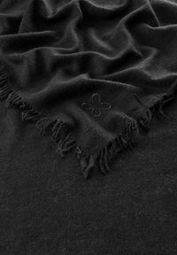 Foulard noir avec des bords à franges, fabriqué en tissu doux, comportant un motif floral en relief. Texture lisse avec un léger éclat.
