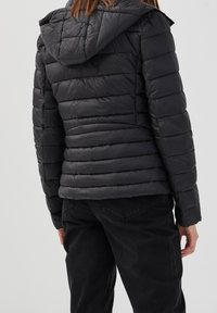 Doudoune noire avec capuche, dotée d'un design matelassé et d'une silhouette ajustée. Fabriquée en matériau léger et brillant.