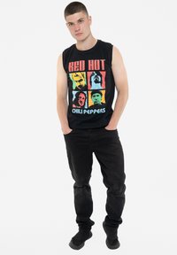 Black sleeveless shirt featuring colorful printed images and text "RED HOT CHILI PEPPERS." Paired with black pants and dark footwear.