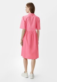 Abito midi in cotone rosa con maniche corte, vita arricciata e colletto. Tessuto morbido e vestibilità comoda con gonna a campana. Sneakers bianche.