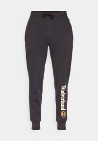 Svarta sweatpants i mjukt tyg med elastisk midja och snörning, avsmalnande ben och en tryckt "Timberland"-logotyp i ljusbeige.