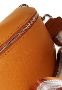 Oranje leren crossbodytas met ritssluiting, een gestructureerd oppervlak en een gestreepte stoffen riem in oranje en beige tinten.