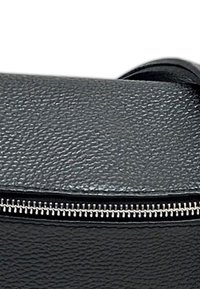 Zwarte lederen tas met een ruwe structuur en een gladde flap. Voorzien van een zilveren ritssluiting langs de rand en een minimalistisch ontwerp zonder extra accenten.