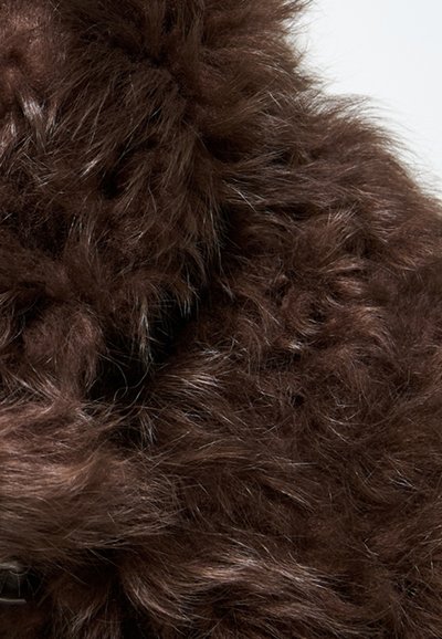 Primo piano di una pelliccia riccia e fluffy di colore marrone scuro, con sottili fili visibili su uno sfondo chiaro.