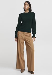 Dark green textured knit sweater with long sleeves paired with tan wide-leg trousers and brown pointed-toe heels.