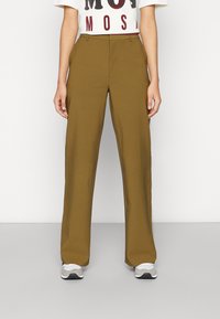 Högmidjade, vida byxor i olivgrön tyg med framveck och en slät textur. Matchas med en kortärmad grafisk t-shirt och sneakers.